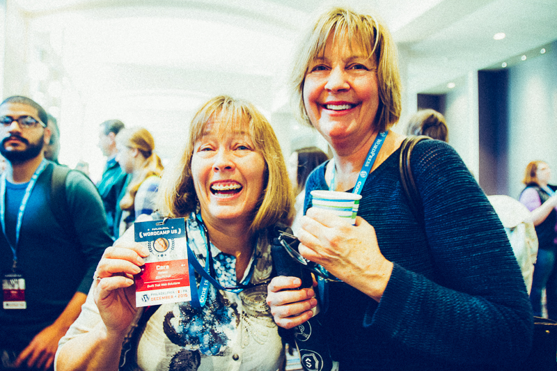 Woman showing her WCUS badge and another holding a cup in a group of attendees.