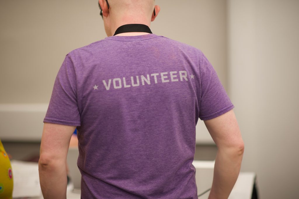 The back of a person wearing a purple shirt with the word Volunteer printed on it