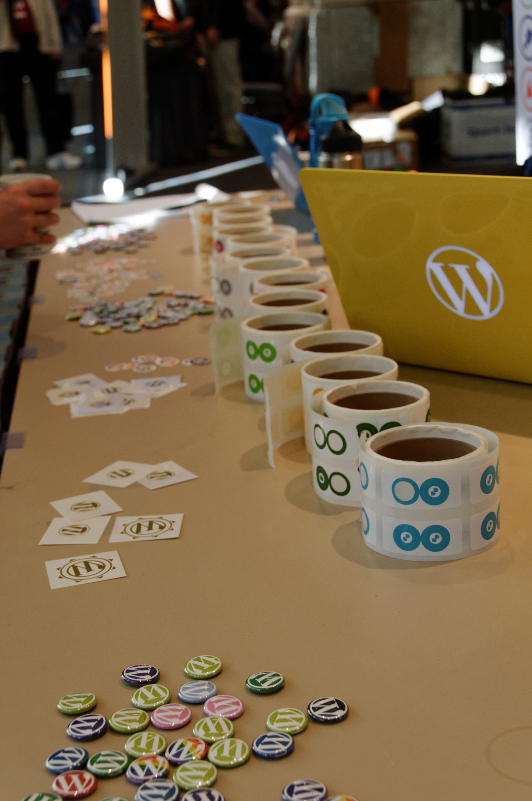 WordPress pins, stickers, and a laptop sit neatly on a table at a WordCamp event