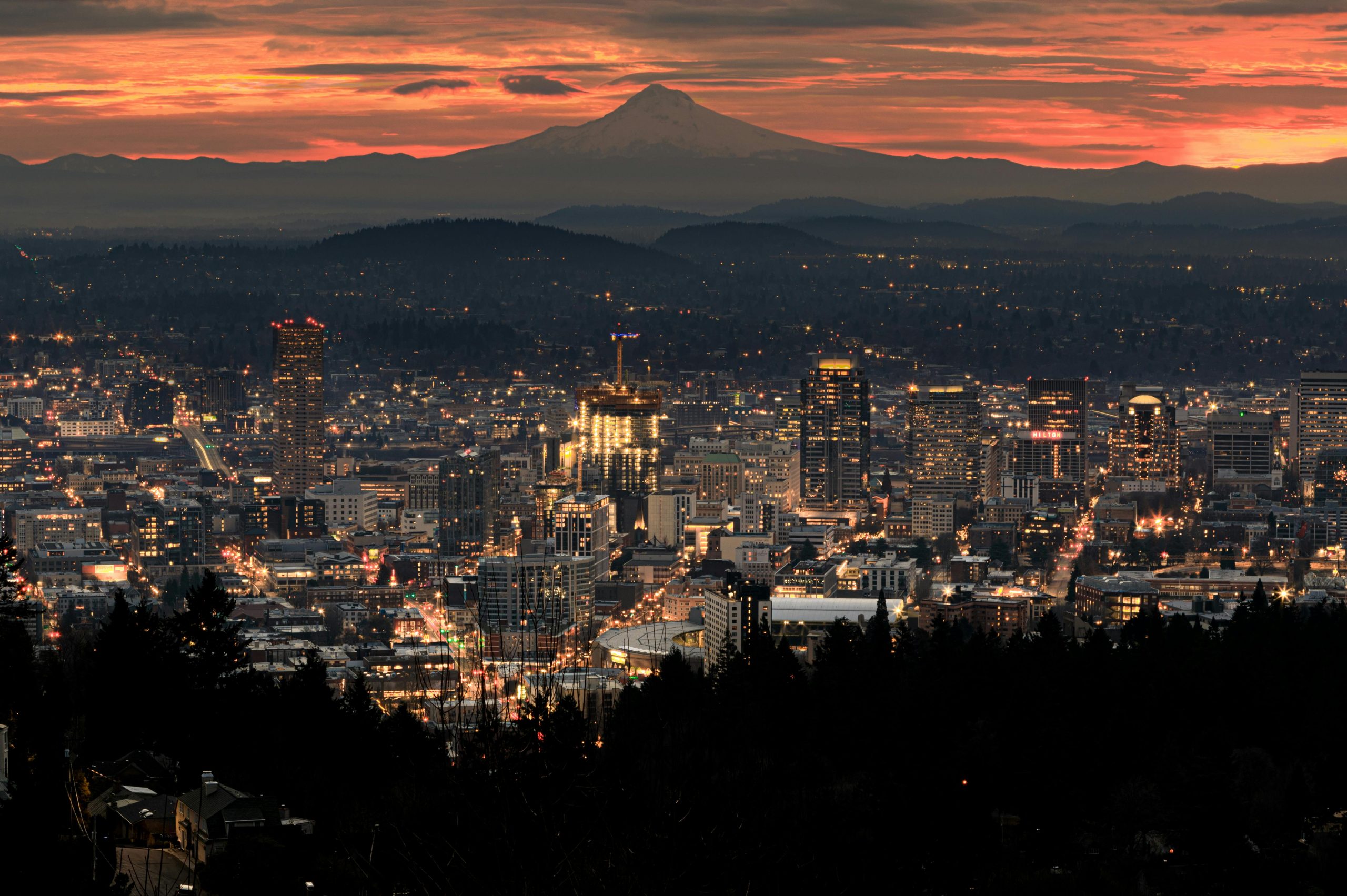 A view at dusk of downtown Portland's skyline with mountains behind it.