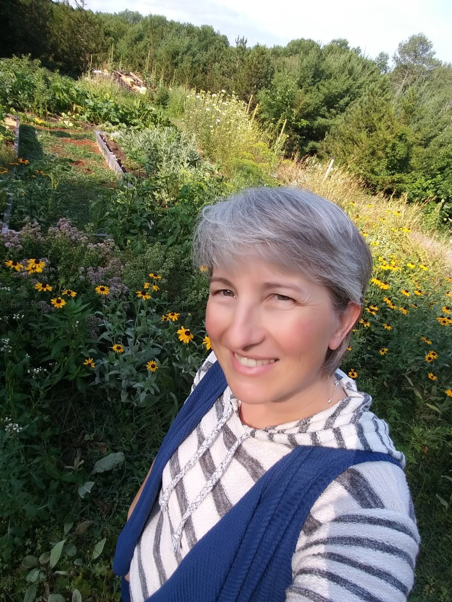 A photo of Cynthia Norman standing in a garden, smiling at the camera.